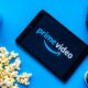 Prime Video logo appears on a tablet surrounded by a can of soda, spilled popcorn, headphones and a cactus