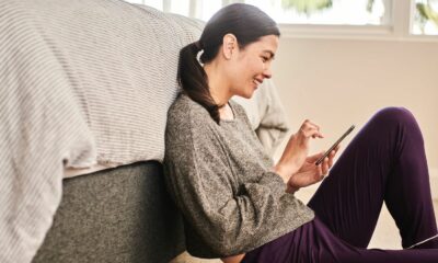 Woman wearing a gray sweatshirt sitting beside her bed and using her smartphone