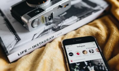 Foto av Instagram på en användares smartphone bredvid en bok och kamera