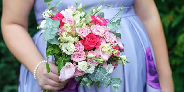 Pregnant bridesmaid wears periwinkle floral dress while holding a bouquet.