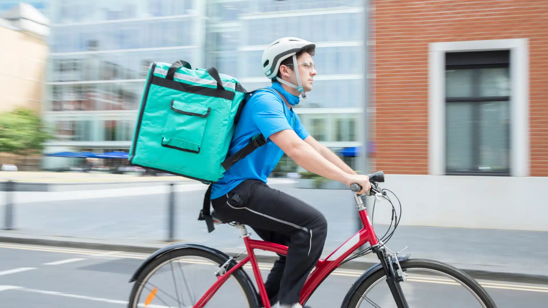 A man riding a bicylce with a food delivery case on his back. 