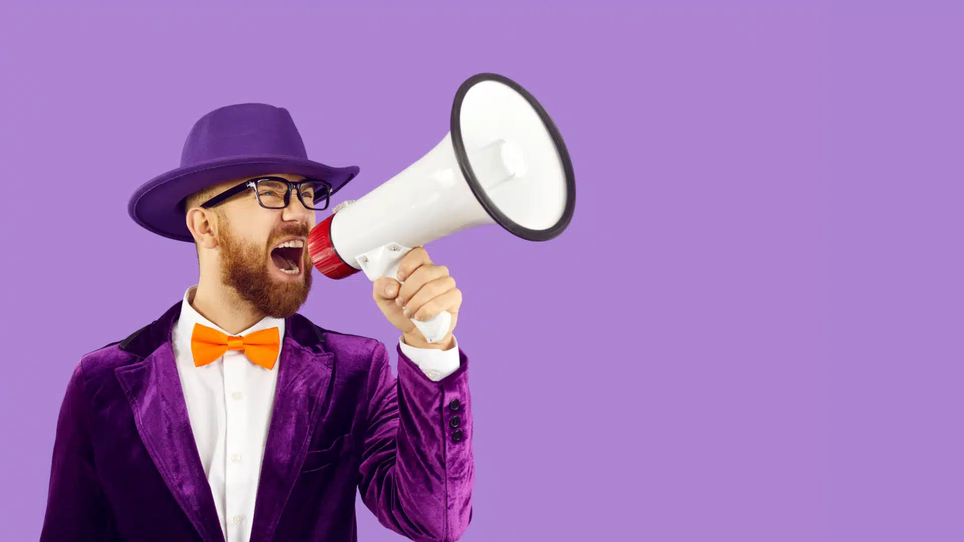 A man in a loud purple suit shouts into a megaphone to promote something. 