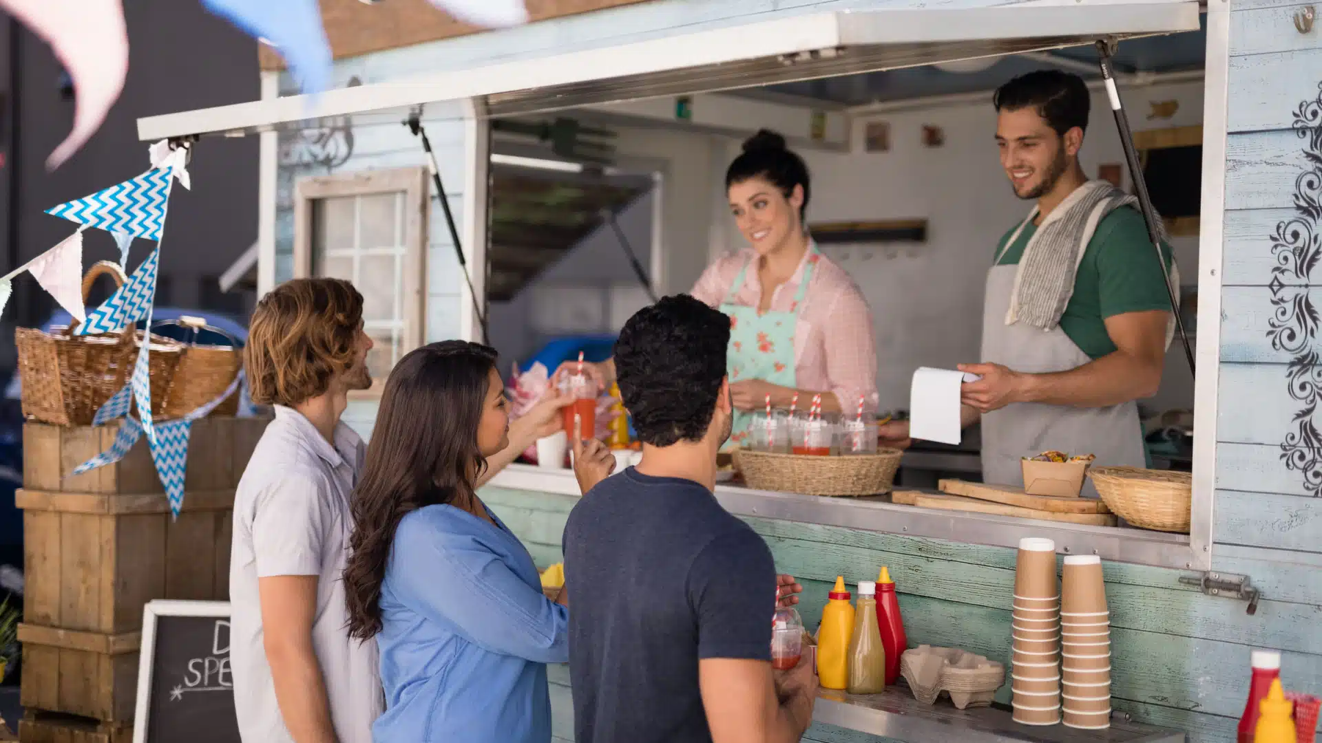 Customers interacting with smilling servers at a food truck. 