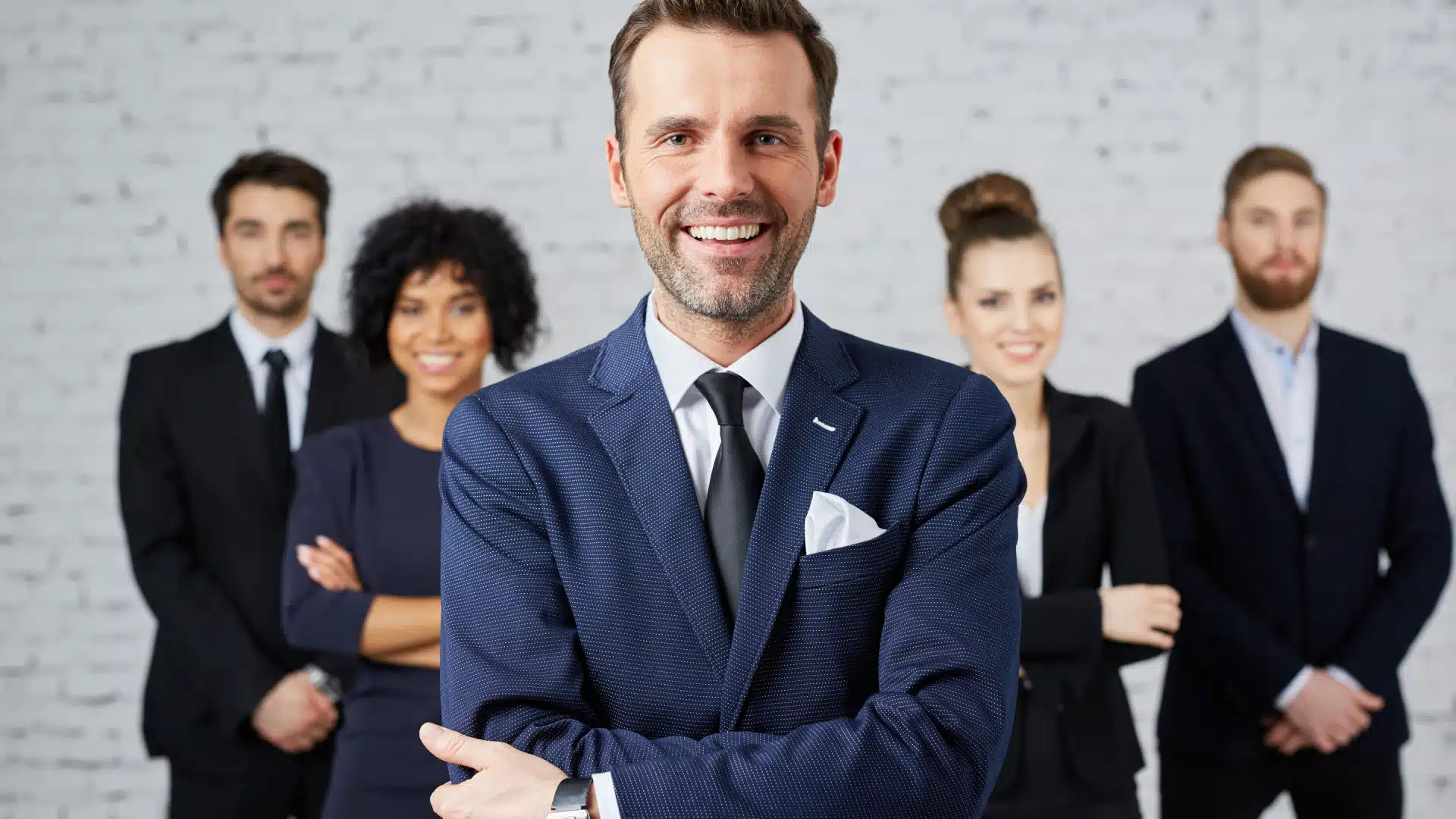 A smiling business man stands in front of his team.