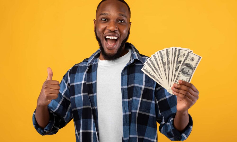 Happy man holding money in one hand giving a thumbs up sign with the other.