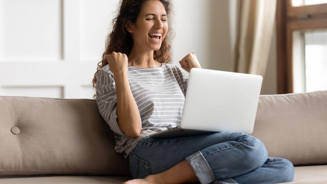 Woman sit on sofa put pc on lap clenched fists scream with joy while read great news on laptop. Gambler celebrate online auction bet victory. Got incredible offer sincere emotions of happiness concept