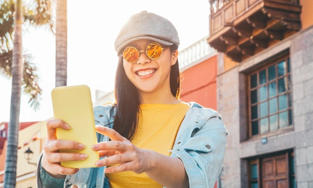 Happy Asian girl using mobile smartphone outdoor - Chinese social influencer having fun making video story for new trends social networks app - People, millennial generation and technology concept stock photo