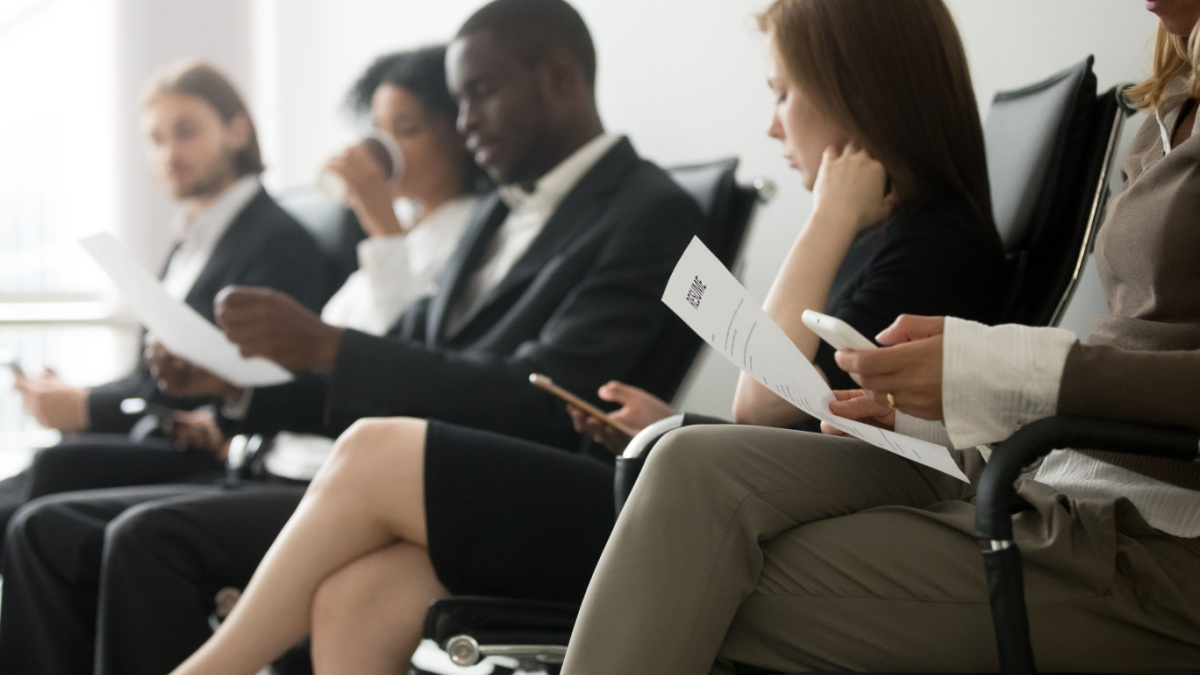 Multi-ethnic applicants sitting in queue preparing for interview, black and white vacancy candidates waiting on chairs holding resume using smartphones, human resources, hiring and job search concept