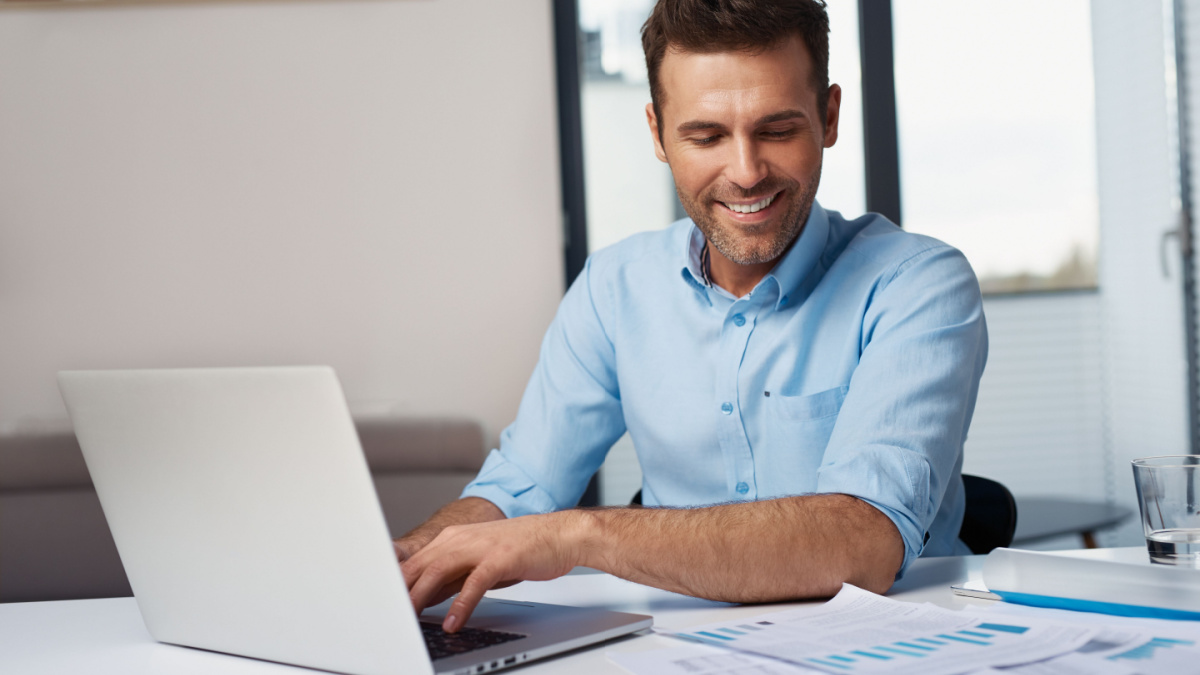 Happy man entering data from home on laptop