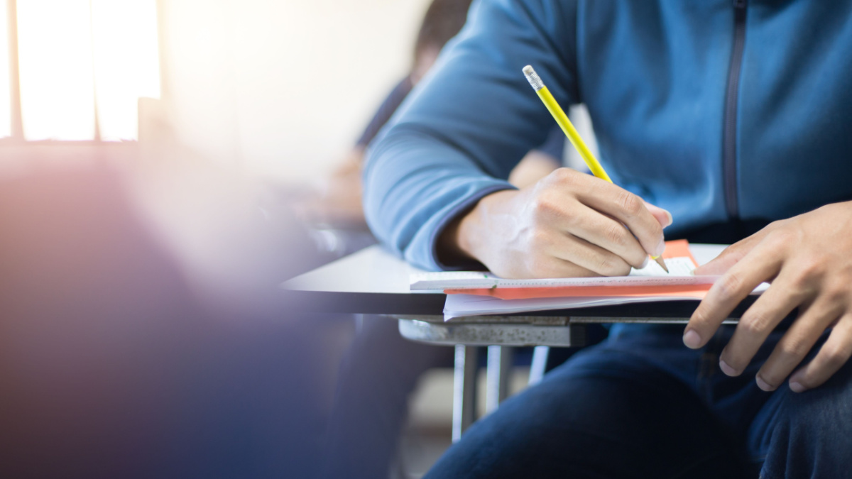 soft focus.high school or university student holding pencil writing on paper answer sheet.sitting on lecture chair taking final exam attending in examination room or classroom.student in uniform.