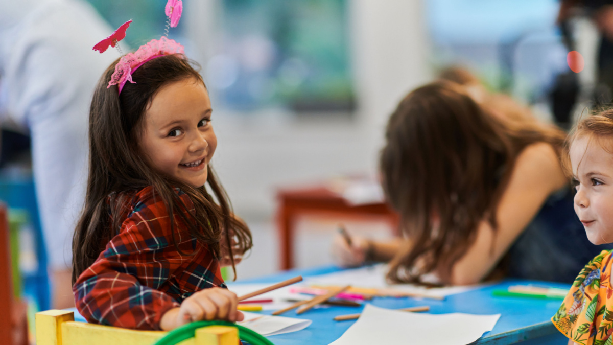 Creative kids during an art class in a daycare center or elementary school classroom drawing with female teacher.