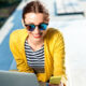 Young woman in yellow sweater working with laptop and phone on the bench in the city.