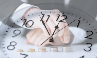 A super rich man in a suit is holding coins in front of a clock.